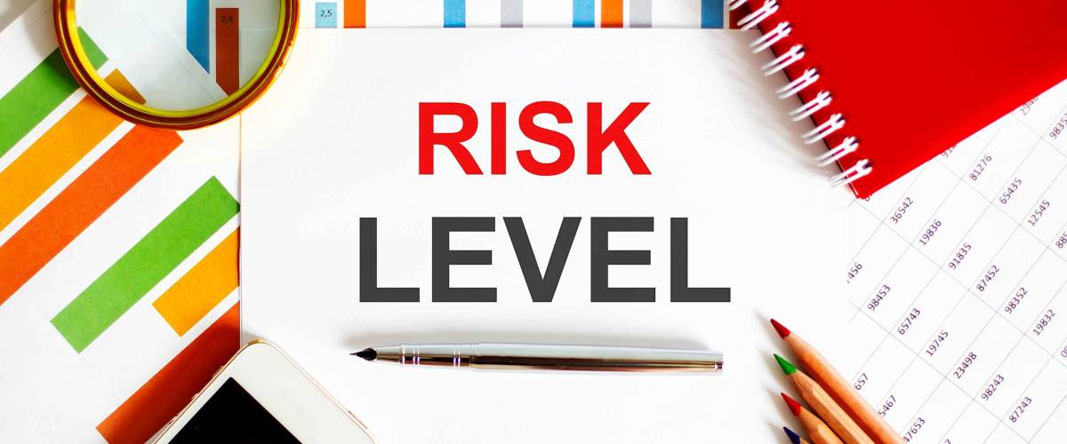 Text RISK LEVEL on notepad with office tools, pen on financial report