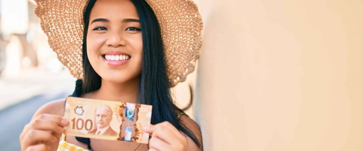 Young asian girl smiling happy at the city holding canadian dollars banknotes