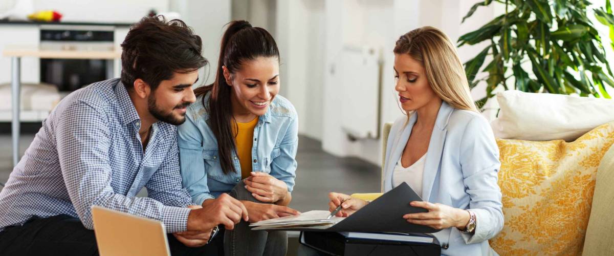 Professional woman shows young couple something on clipboard, everyone smiling.