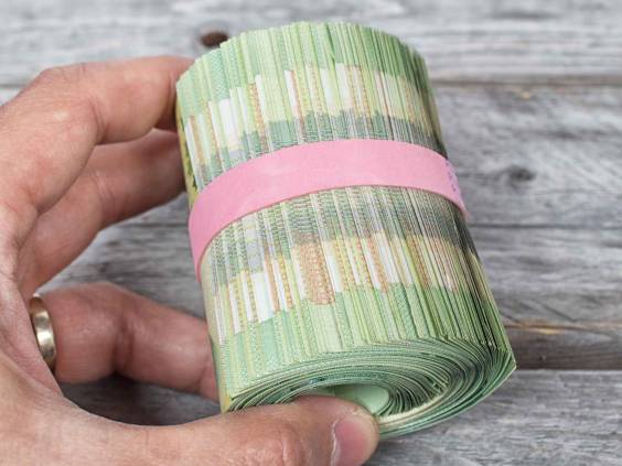 Hand holding a roll full of green bank notes against a wooden background