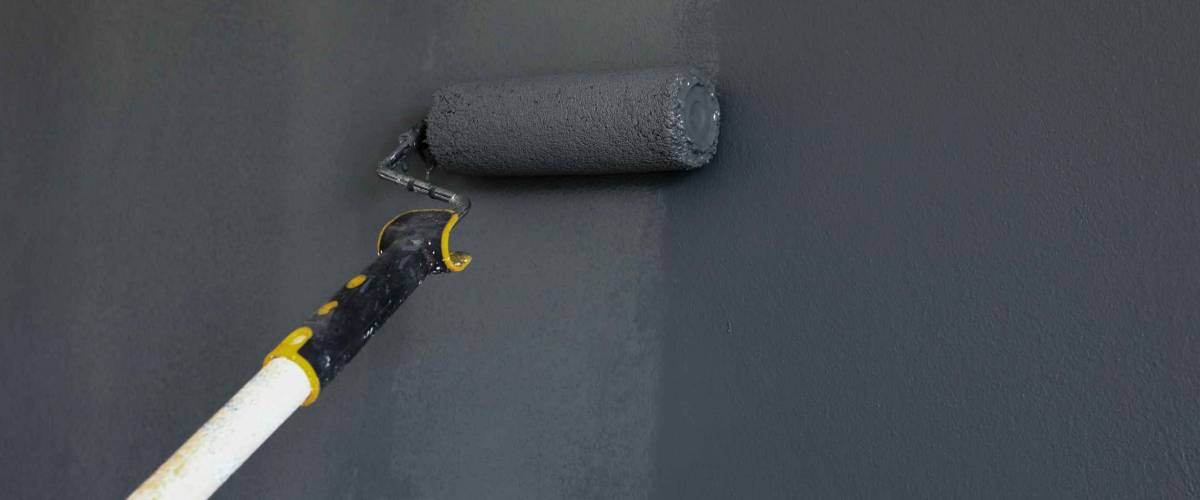 Taking photo of painter using roller painting wall in dark grey color.