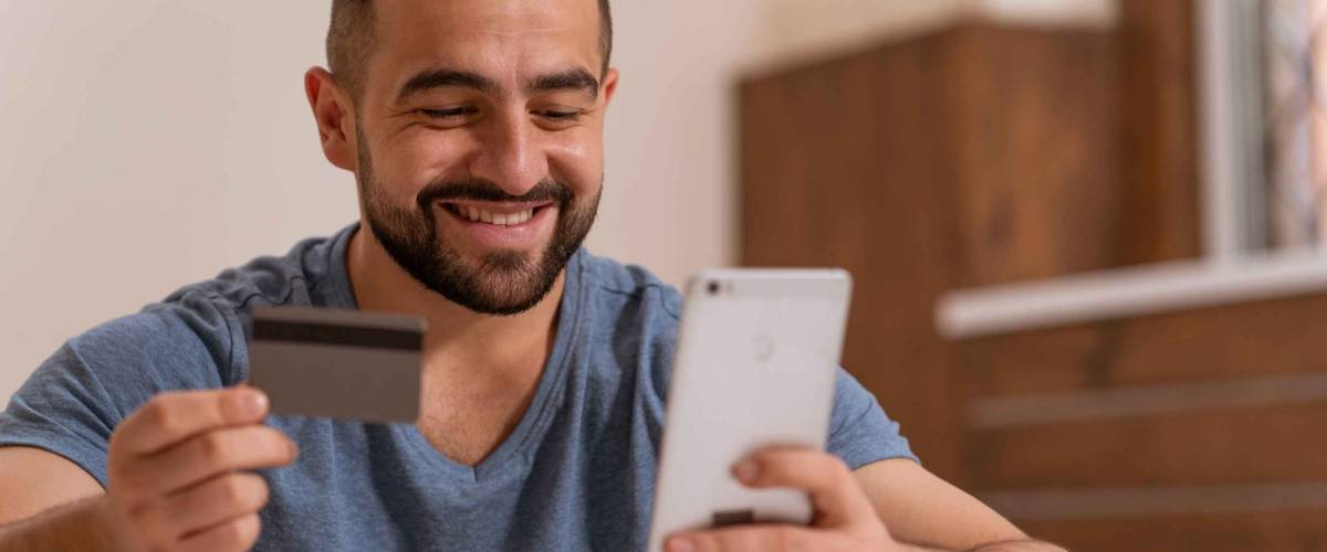 Handsome happy man with smartphone and debit or credit card buying online equipment or doing sport bets and gambling online. Modern digital sports life. Sport app on smartphone.