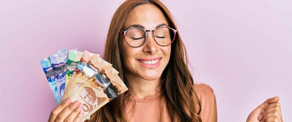 Young brunette woman holding canadian dollars screaming proud, celebrating victory and success very excited with raised arm