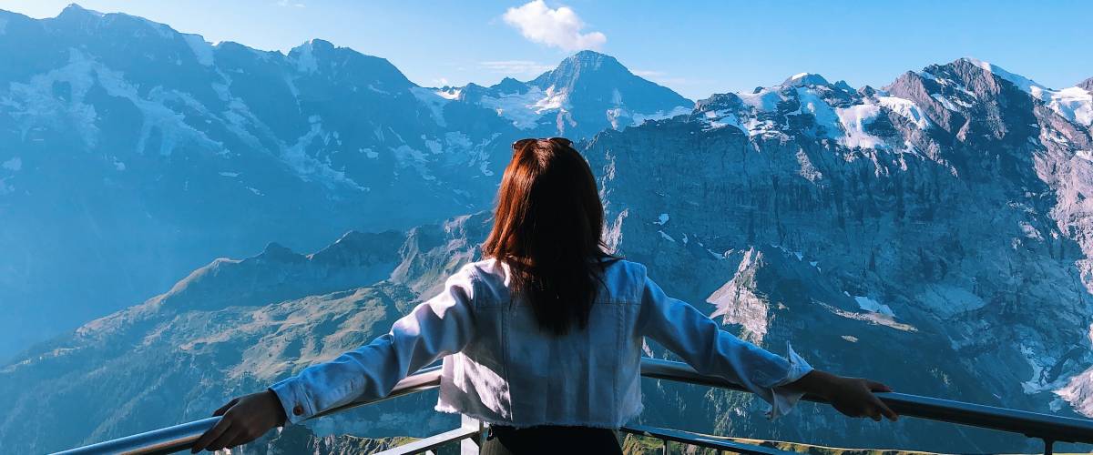 Woman stands on a balcony looking out at mountains