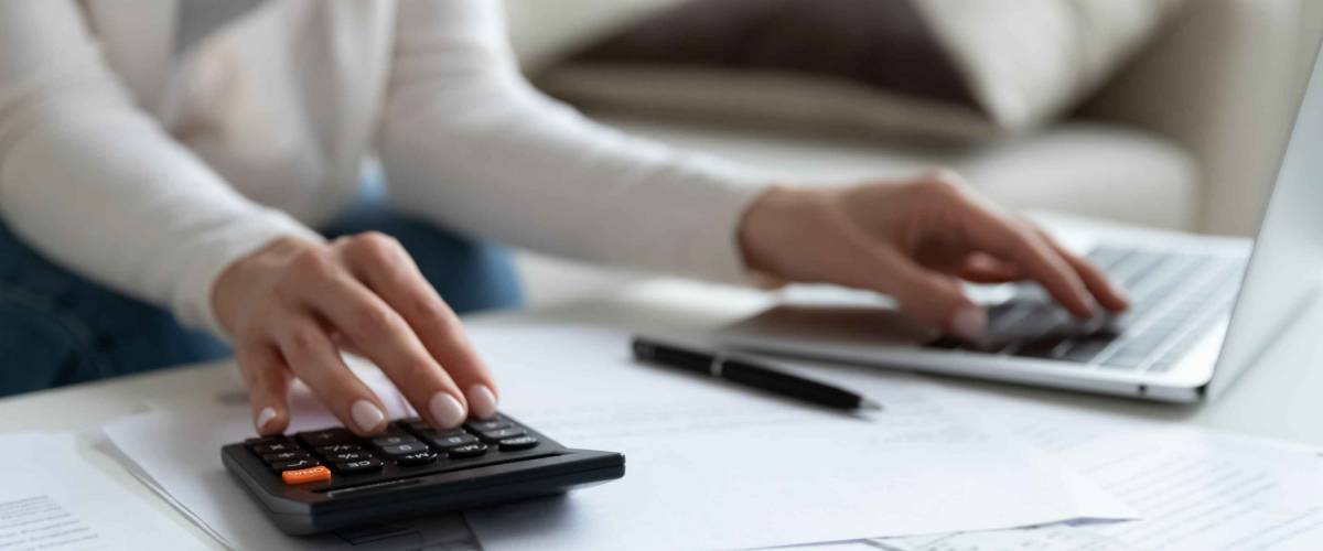 Close up of woman busy paying bills online on computer calculating household finances or taxes on machine, female manage home family expenditures, using calculator, make payment on laptop