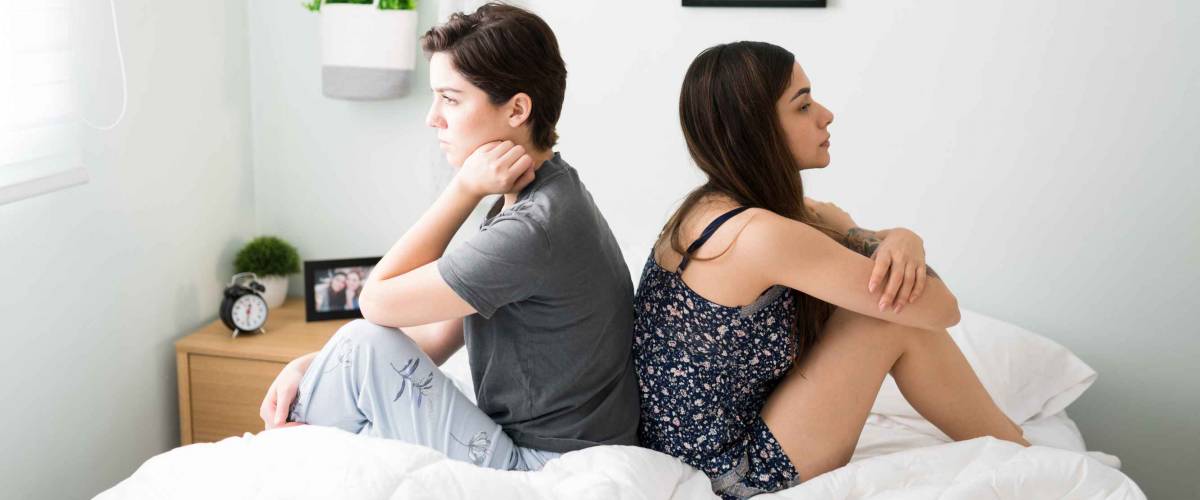 Angry lesbian couple fighting while sitting in bed during the morning. Gay attractive women with their backs turned and having a discussion