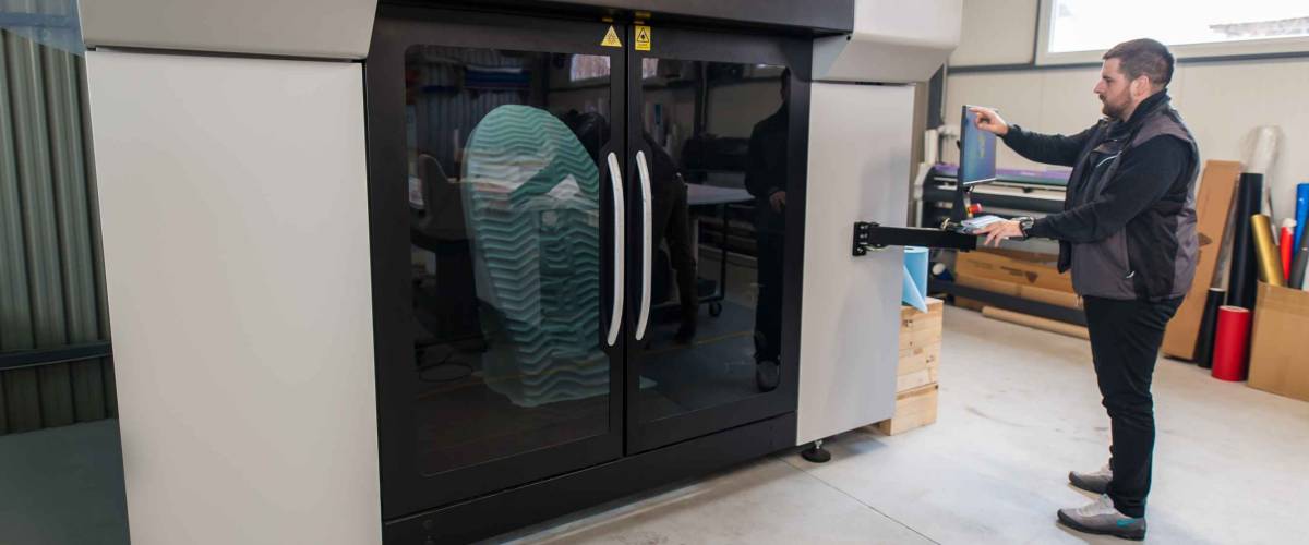 Printshop worker printmaker technician works on large modern 3d printer machine with computer control