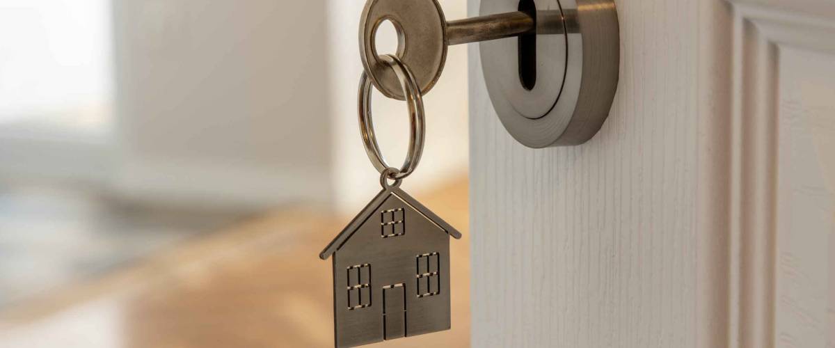 Open door to a new home with key and home shaped keychain. Mortgage, investment, real estate, property and new home concept
