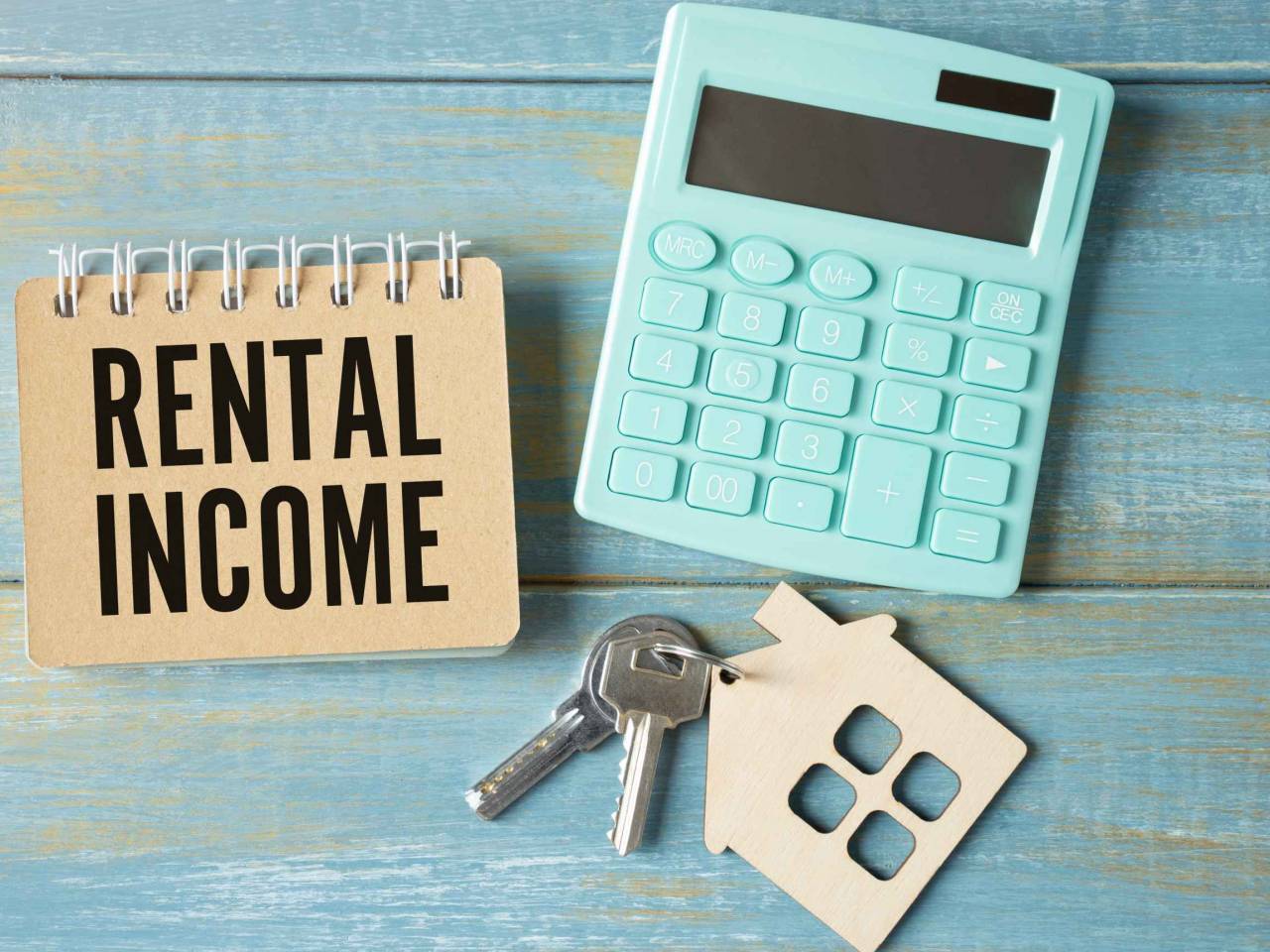 The word rental income is written in a notebook that sits on a gray desktop along with a laptop. Business image