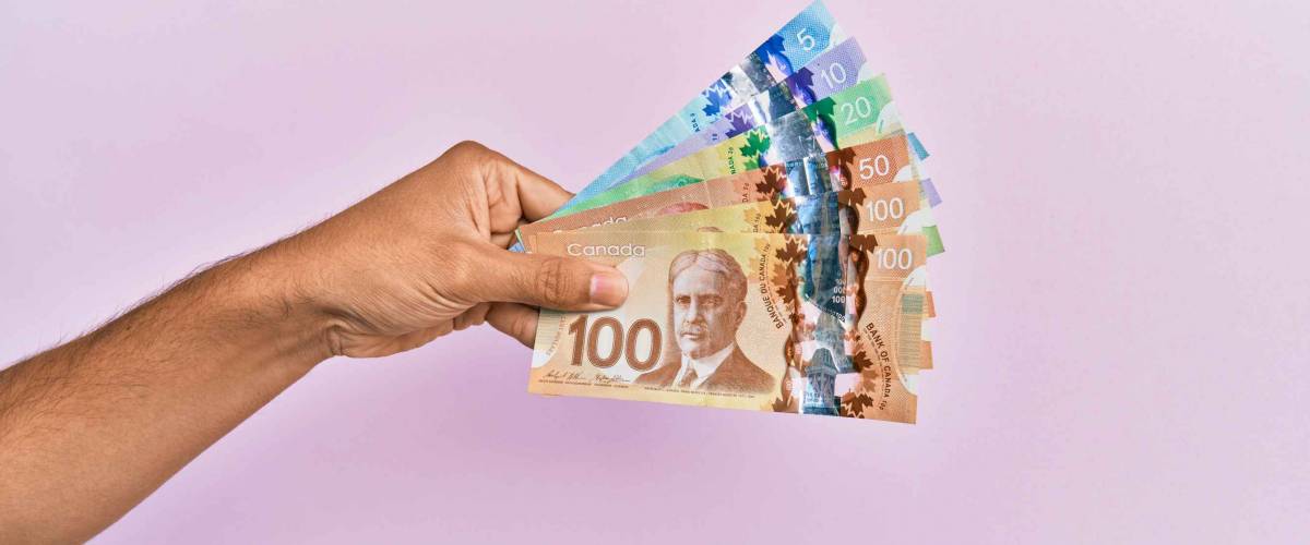 Hispanic hand holding canadian dollars banknotes over isolated pink background.