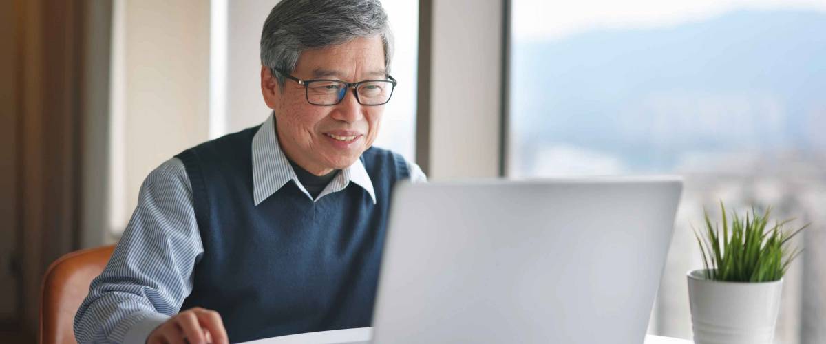 Asian senior businessman uses laptop to work near window at home