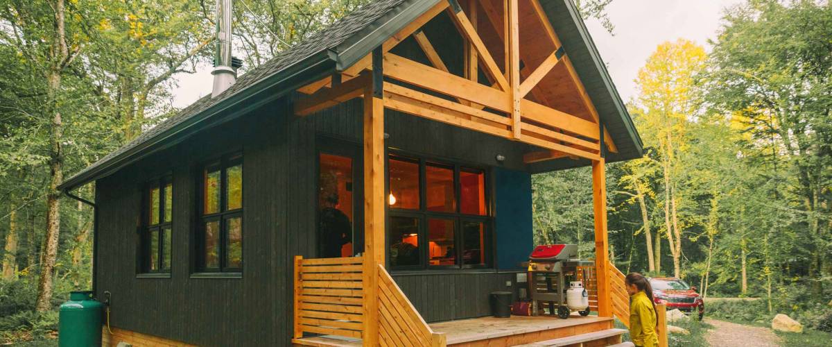 Vacation rental forest lodge countryside cabin by the lake for holidays in the wilderness. Woman entering her house home away from home.