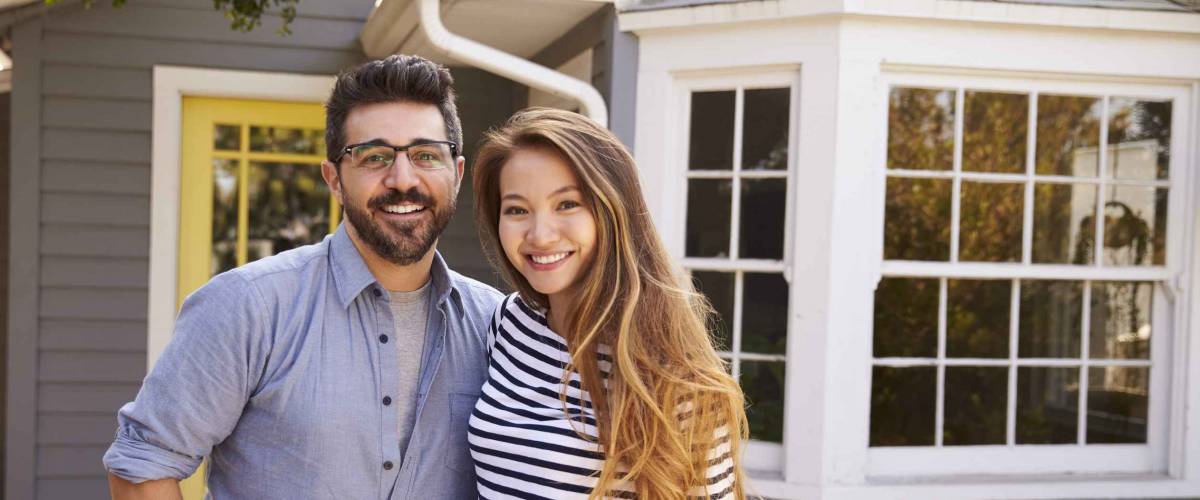 Portrait Of Excited Couple Standing Outside New Home