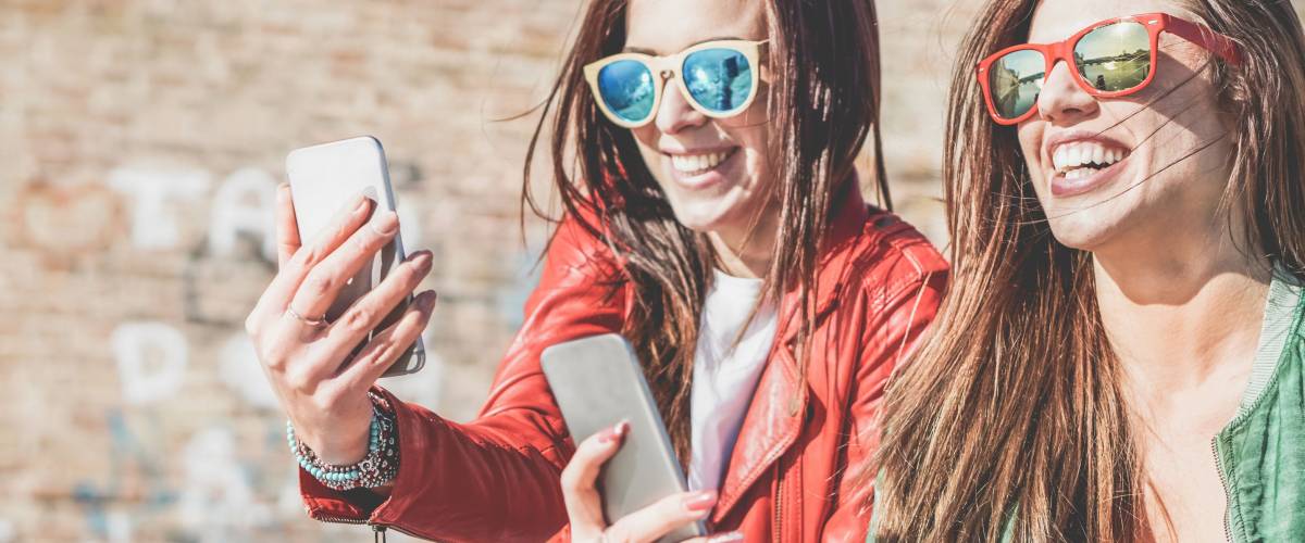 Happy fashion friends watching videos on smartphone - Girlfriends having fun social technology trends outdoors - Friendship, youth lifestyle, millennials generation and tech concept
