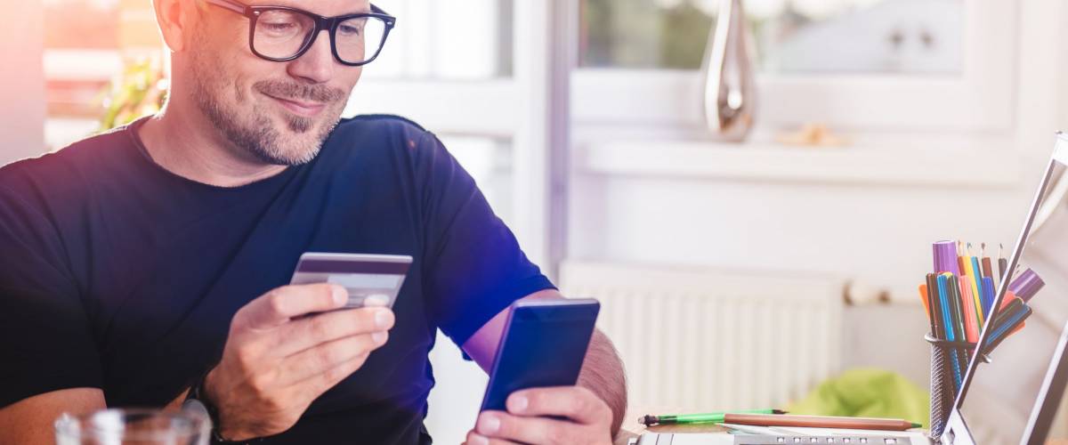 Man paying with credit card on smart phone at home office