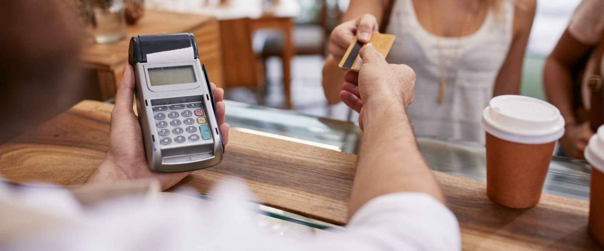 Customer paying for their order with a credit card in a cafe. Bartender holding a credit card reader machine and returning the debit card to female customer after payments.