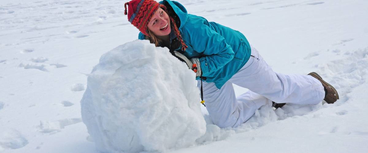 Young college-age woman rolling giant snowball to make snowman