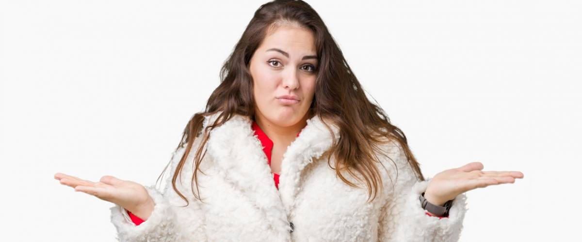 Beautiful plus size young woman wearing winter sheep coat over isolated background clueless and confused expression with arms and hands raised. Doubt concept.