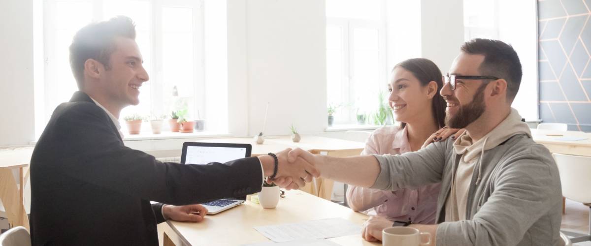 Happy millennial couple and smiling financial advisor, lawyer or realtor shaking hands at office