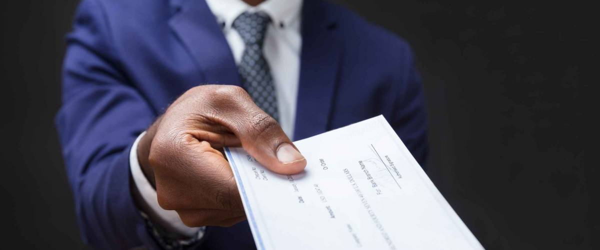 Close-up Of A Businessman's Hand Giving Cheque Over Wooden Desk