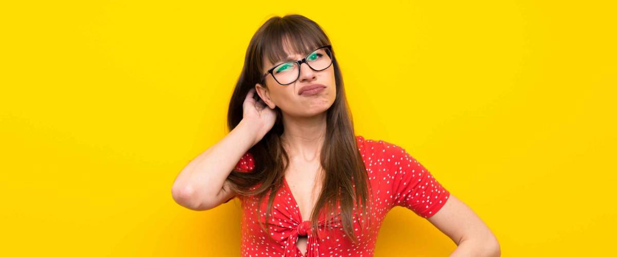Young woman over yellow wall having doubts