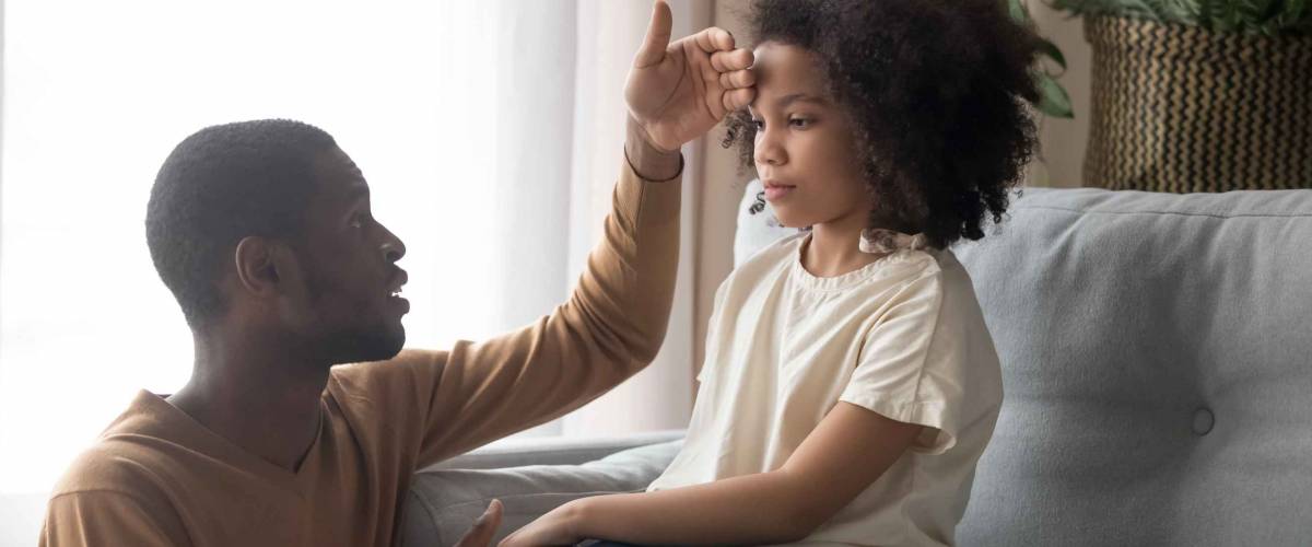 Worried dad father check temperature touch forehead of unhealthy schoolgirl daughter sitting on sofa at home