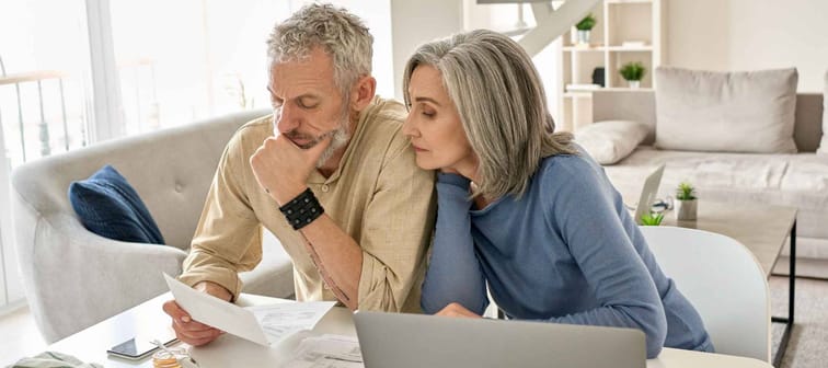 Worried old senior couple checking bank documents at home.