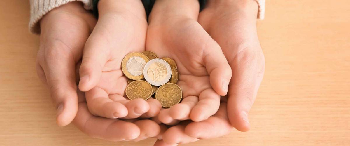 Hands of young man and his son holding coins on wooden table. Concept of child support