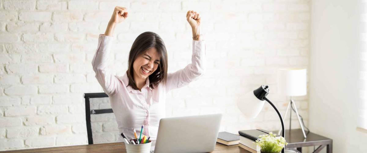 Excited woman using the computer and celebrating some good news with her arms up