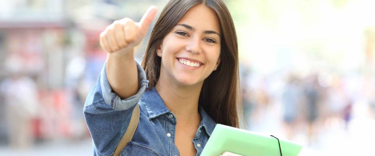 Happy student posing with thumbs up looking at you in the street