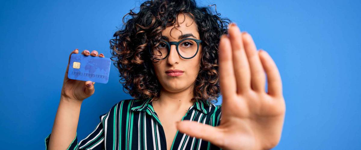 Young beautiful curly arab woman wearing glasses holding credit card money for payment with open hand doing stop sign with serious and confident expression, defense gesture