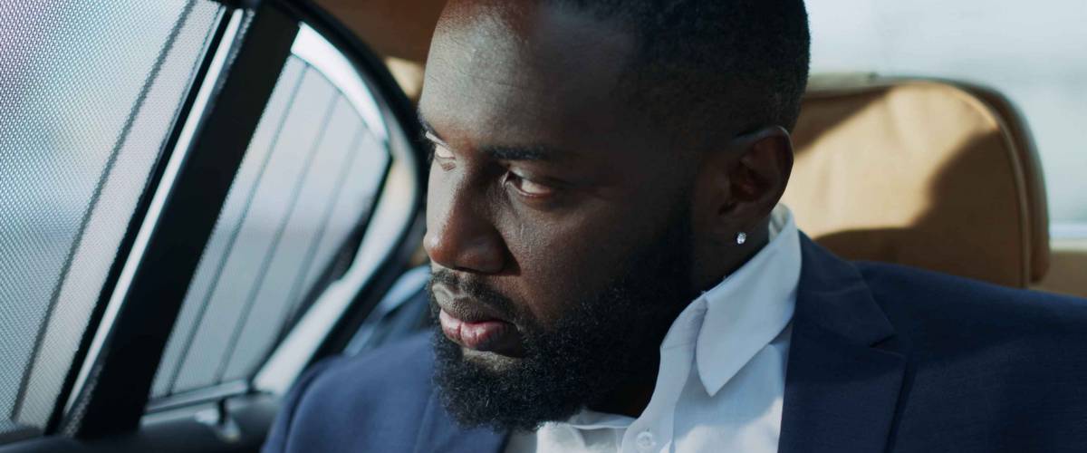 Closeup worried business man feeling stressed at vehicle. Portrait of puzzled african businessman looking away at car window. Sad african man sitting at backseat at car.