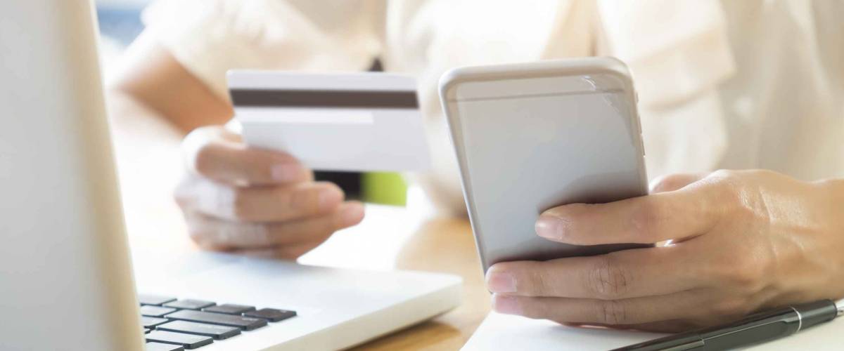 Woman using laptop and mobile phone to online shopping and pay by credit card. This picture is focus at woman's hand and use warm bright sunlight filter for feeling comfortable