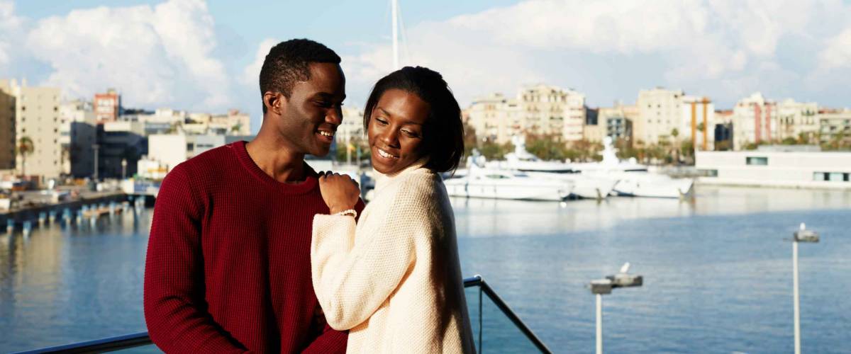 Portrait of happy hugging couple on modern balcony with beautiful port with yachts on background, fashionable couple enjoying each other during vacation holidays in Barcelona