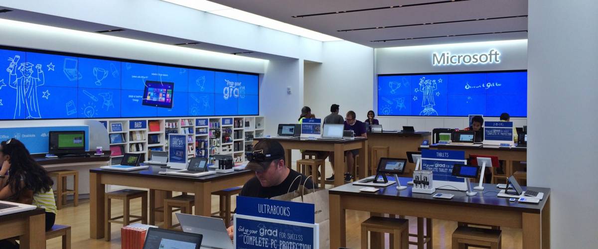 Inside a Microsoft store, with assortment of computers, gadgets, staff and customers