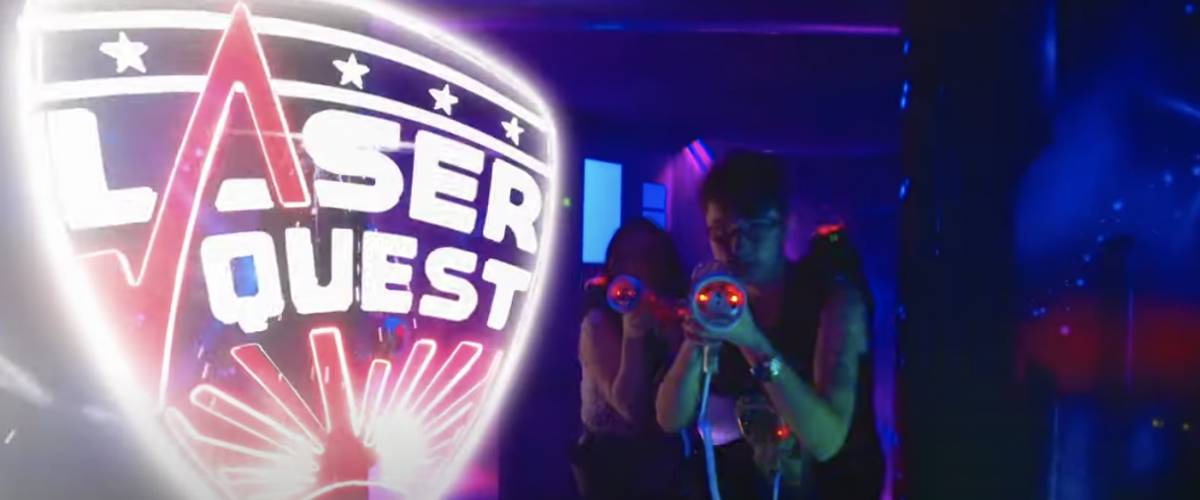 Two people walk with laser guns inside the Laser Quest arena