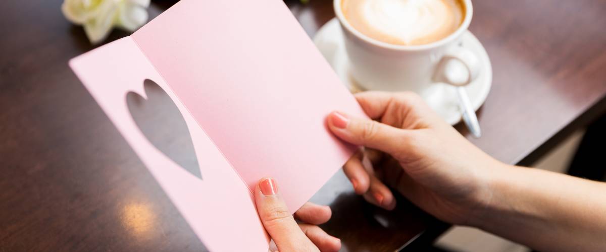 Closeup of hands holding greeting card sitting at table with coffee