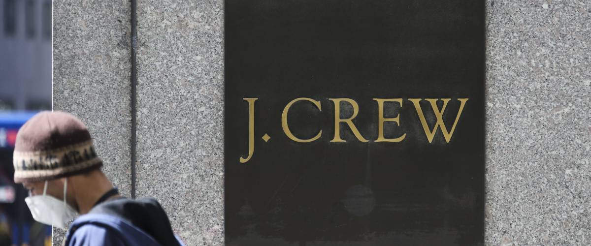 Man wearing a face mask walks past a sign for J. Crew