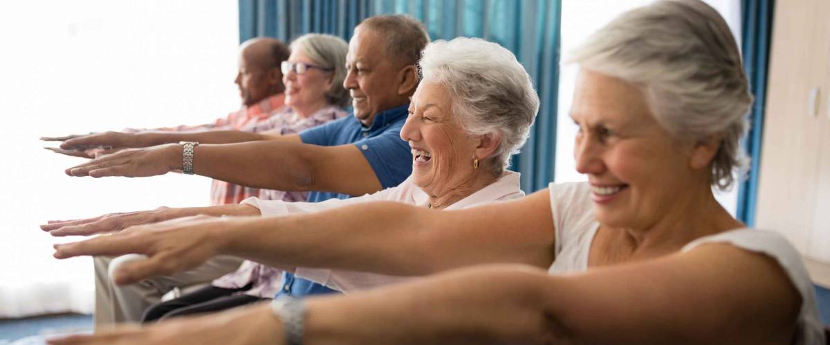 Cheerful senior people exercising with arms raised at retirement home