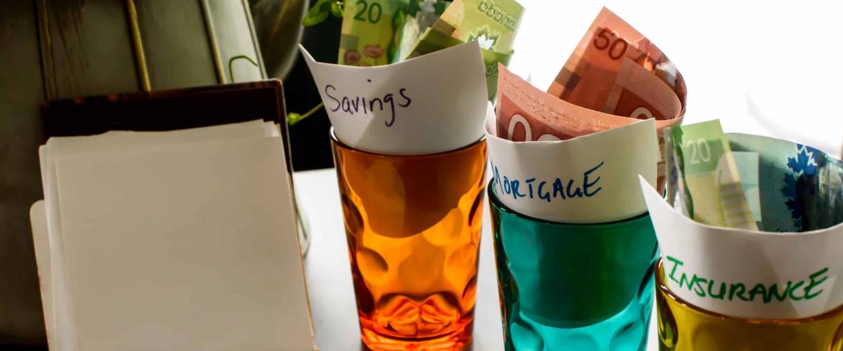 Home budget conceptual photography background notepad on table with glass jars and cash money and words Insurance, mortgage and savings written on paper