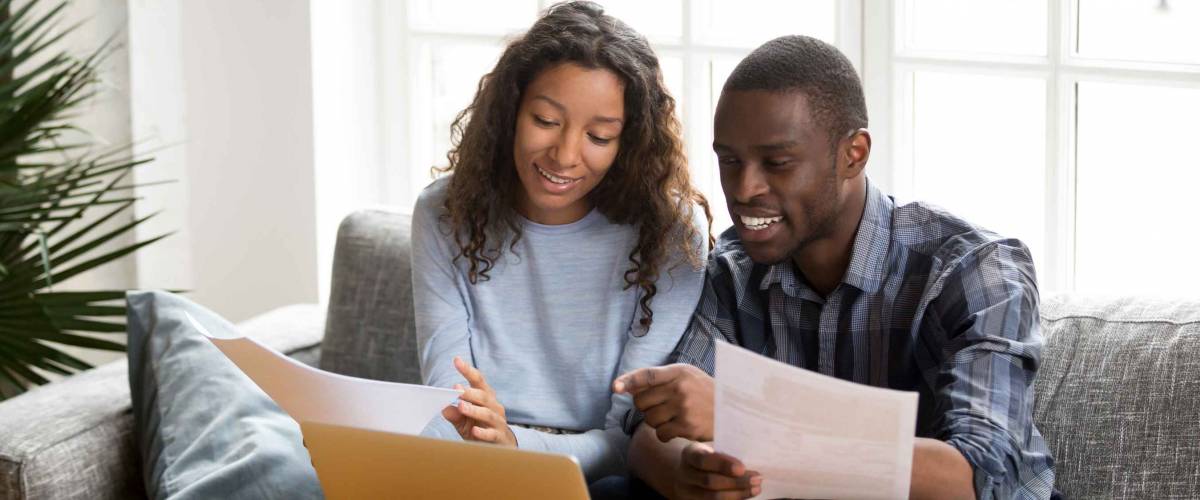 Black positive married couple sitting on sofa at home read documents
