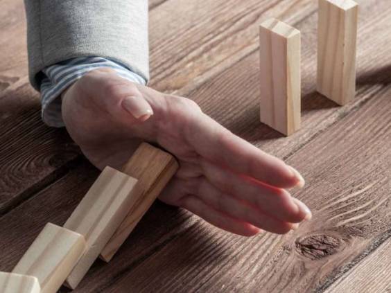 Businesswoman protecting dominoes from falling on wooden desk. Business assistance and leadership in crisis. Operative business solution and stabilization of situation.