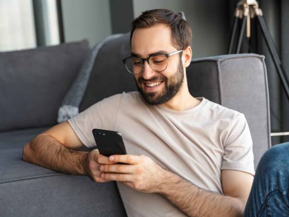 Séduisante jeune homme intelligent assis sur un sol dans le salon, à l'aide de téléphone mobile