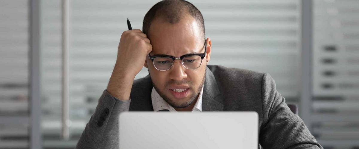 Unhappy African American businessman looking at laptop screen, annoyed employee intern working on difficult online project task, sitting at office desk, receive bad news, notification