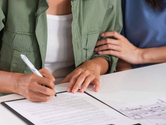 Close up of two people sitting at a desk, signing a piece of paper.