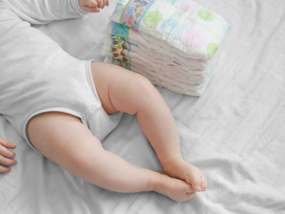 Baby feet and a pack of diapers on a white bed.