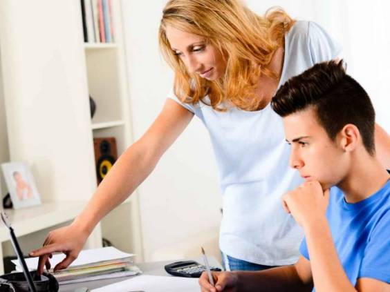 cheerful young woman teacher helping a teenager doing homework