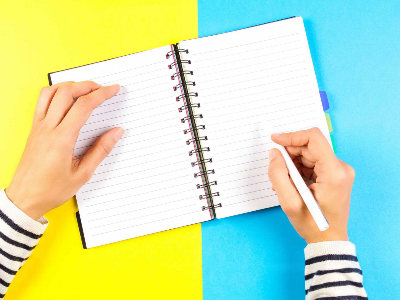 Woman hand writing in notebook over blue and yellow background.