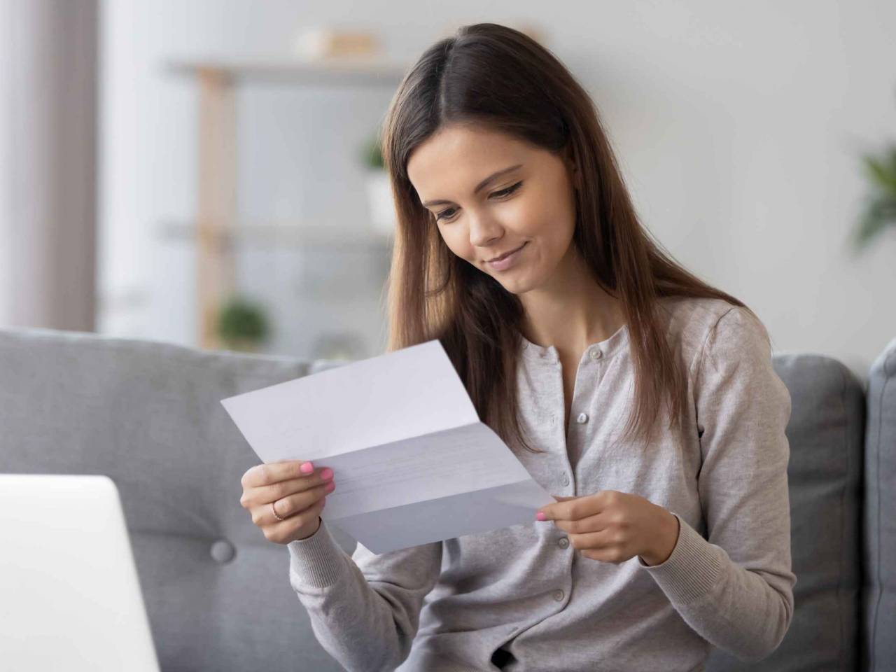 Young attractive woman sitting on sofa at home holds paper reading letter