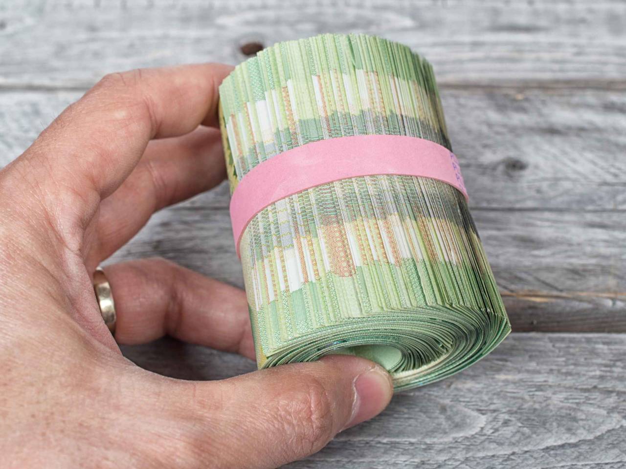 Hand holding a roll full of green bank notes against a wooden background